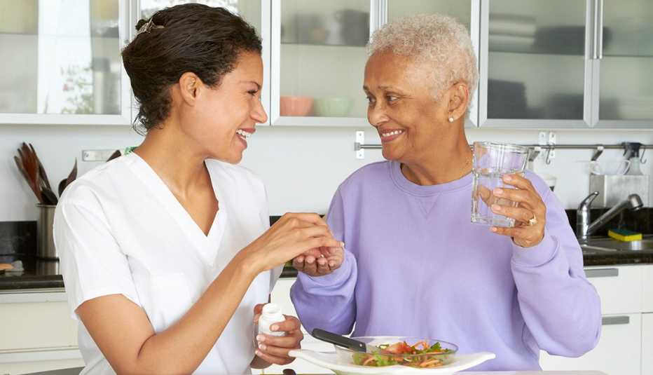 Home health aide giving her female care recipient her pills and a plate of lunch