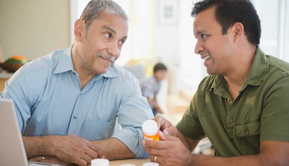A man holding a prescription pill bottle explaining the medication to his father