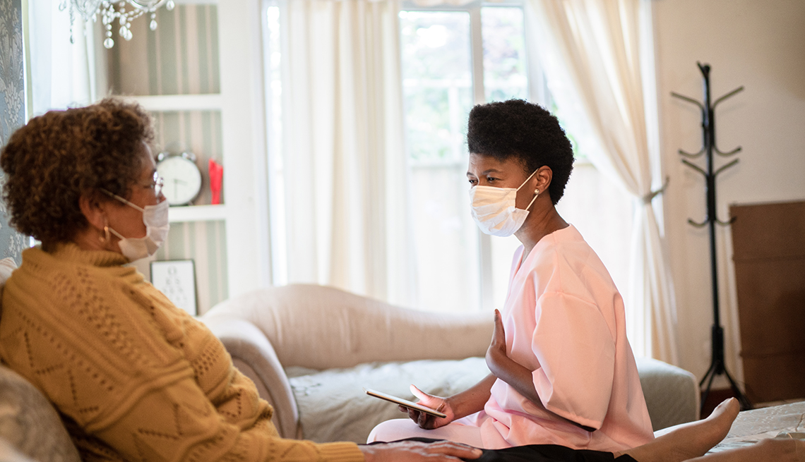 a death doula wearing a face mask talking to her patient as she lies in bed