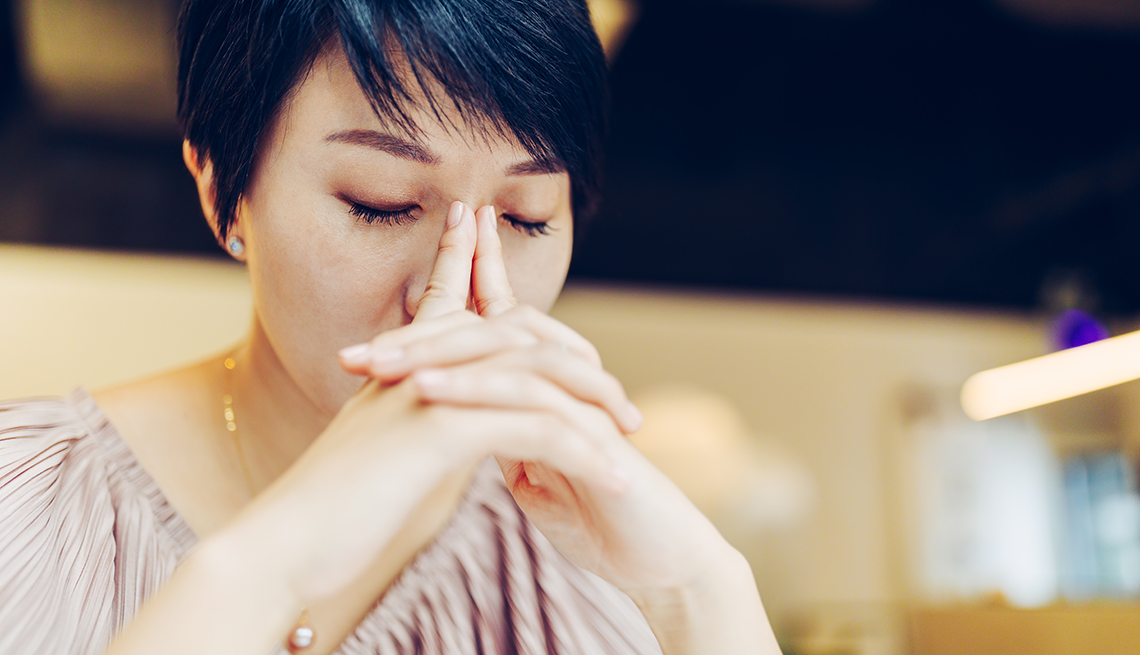 a stressed looking woman with her eyes closed and hands folded near her face