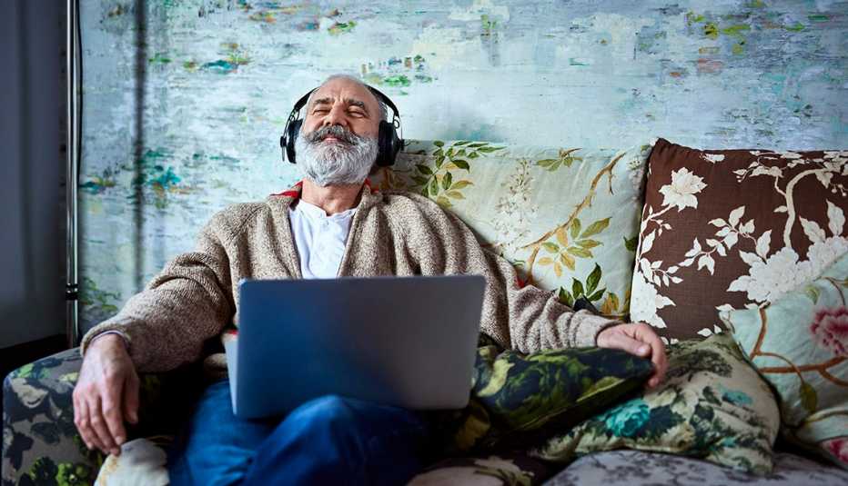 Male family caregiver relaxing on his couch listening to music through headphones