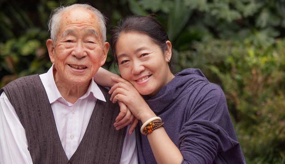 An older man smiling with his daughter's arms on his shoulder