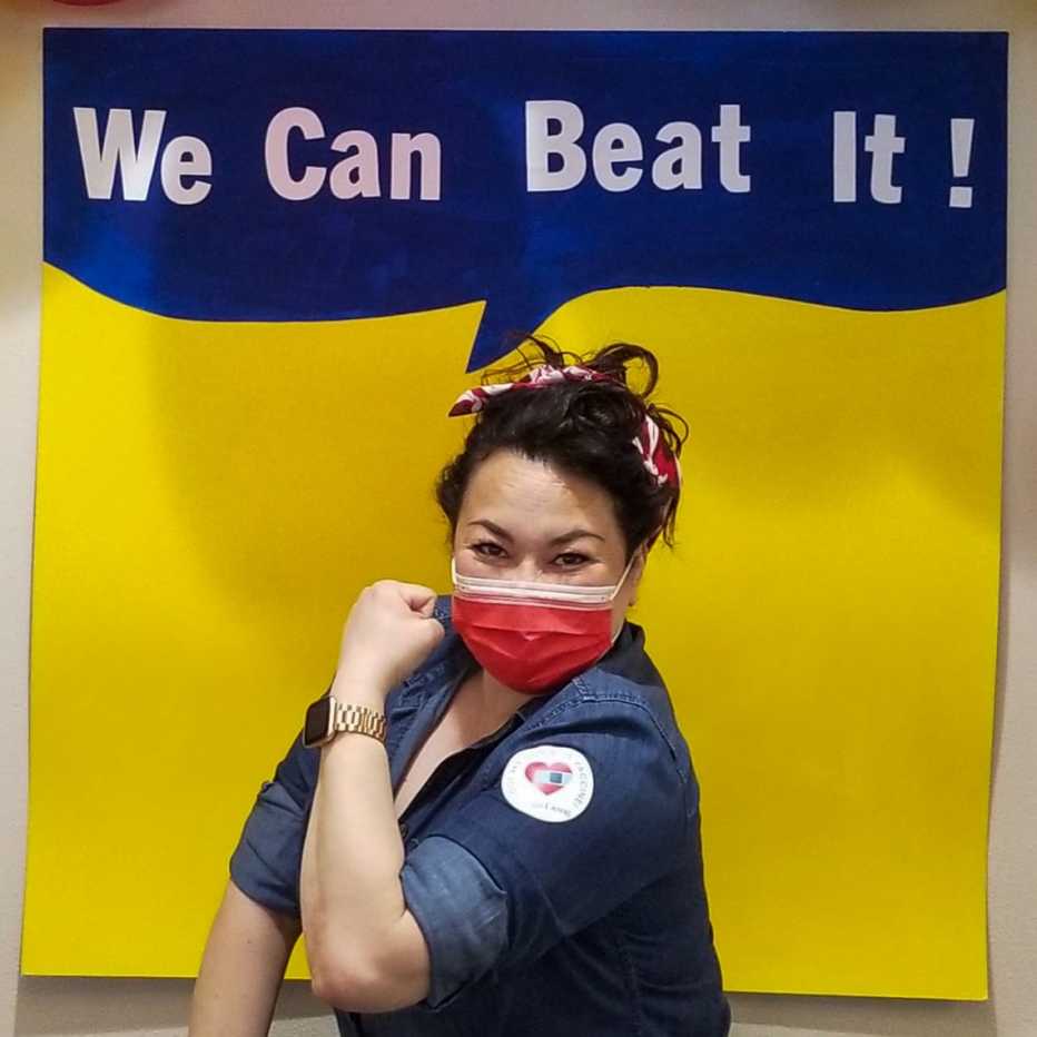 a nursing home worker posing as rosie the riveter with a vaccine sticker on her arm