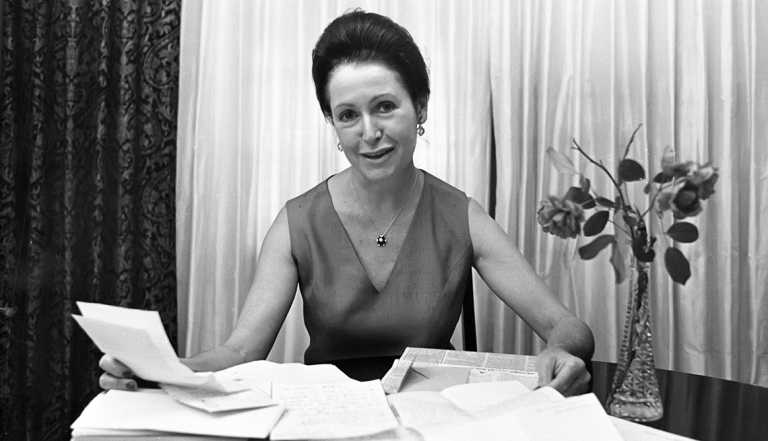 Mary Higgins Clark sitting at table with papers in front of her, vase with flowers to the side