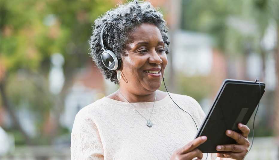 Close up of a senior, African American woman wearing headphones and using a digital tablet.  She could be listening to music or an audio book.