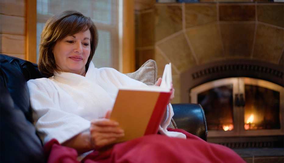 woman sitting on a couch, reading a book by the fire