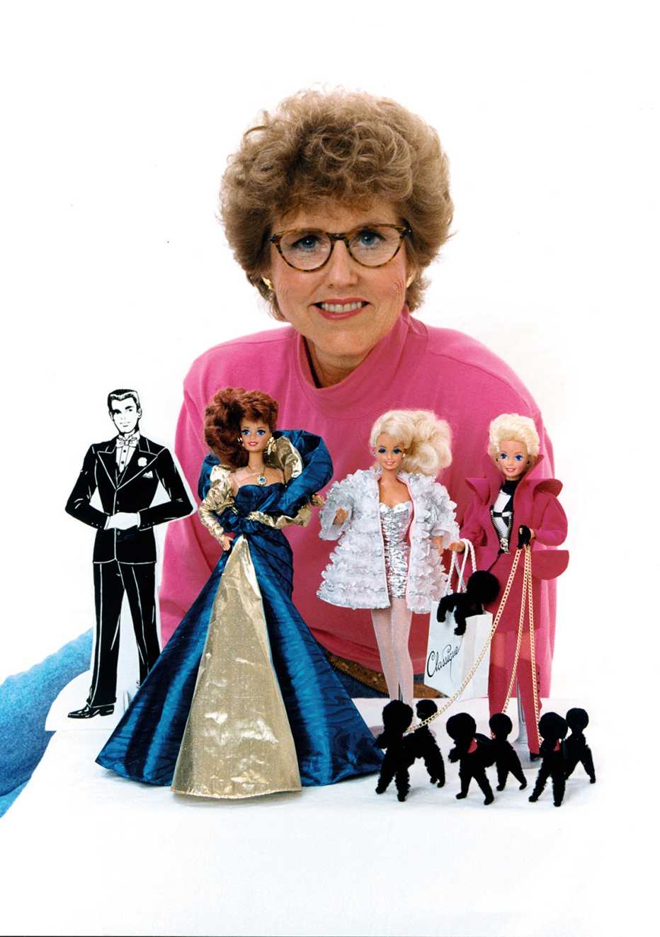 carol spencer sitting behind three barbie dolls and a small paper cutout of ken