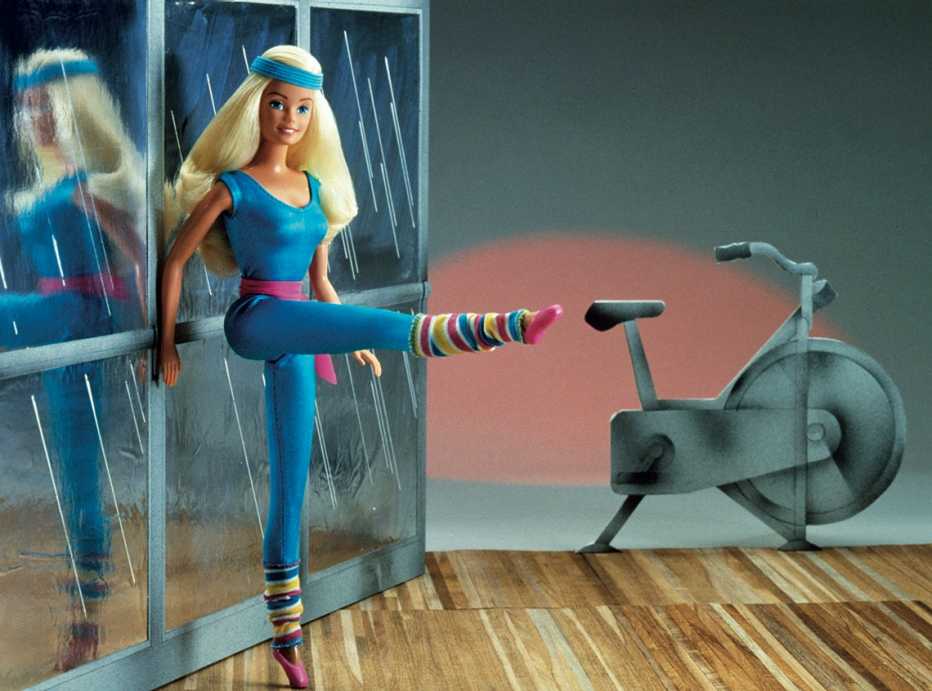 a barbie doll in aerobics apparel in a gym with a model exercise bike in the background