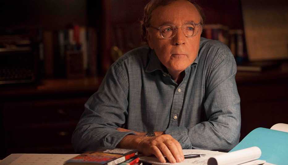 author james patterson looks off camera while sitting at a desk holding a pen