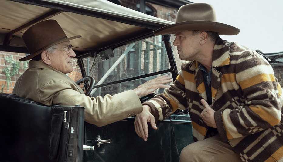 robert de niro sitting in a car while talking with leonardo dicaprio standing outside of the vehicle in a scene from the film killers of the flower moon