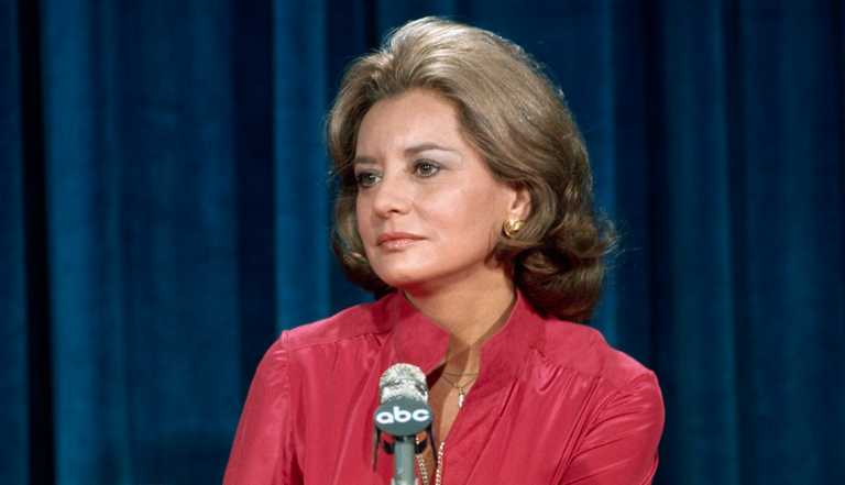 Barbara Walters in her 40s in front of dark blue curtain with A B C microphone in front of her
