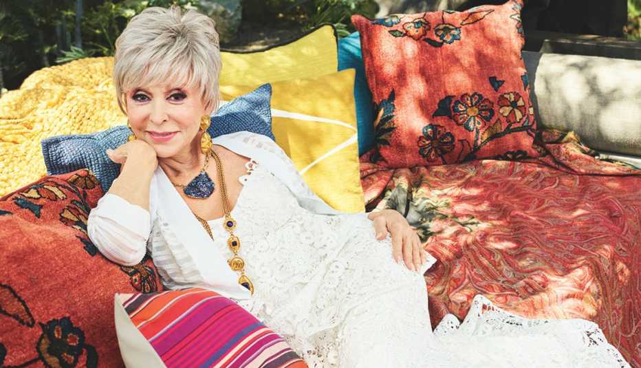 Rita Moreno sitting on a couch outside.