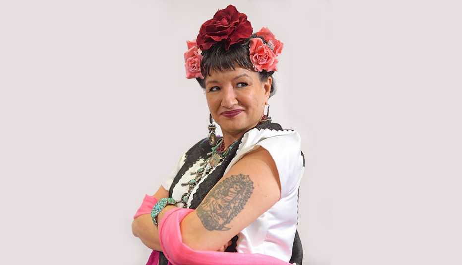 Sandra Cisneros, with flowers in her hair and a tattoo on her arm, looking to the side.