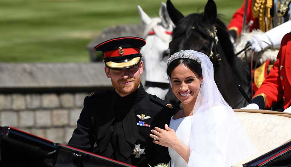 Prince Harry and his wife Meghan, Duchess of Sussex, sit next to each other in a carriage and look at a procession crowd.