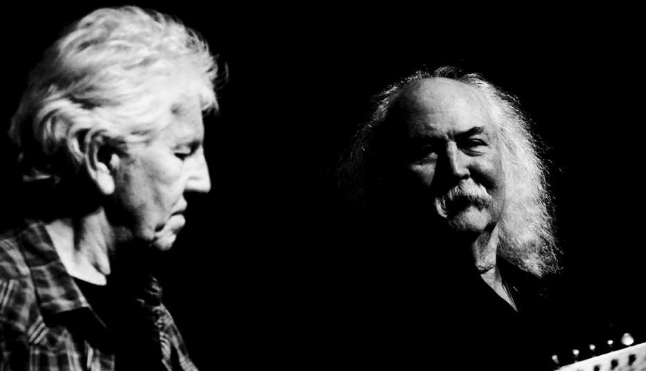 Graham Nash playing the guitar as David Crosby look on next to him