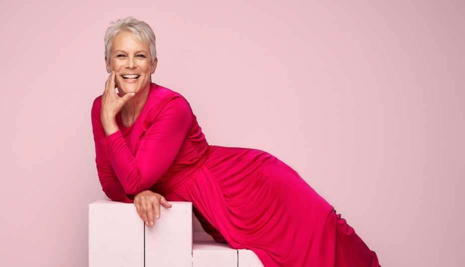 actress jamie lee curtis in a hot pink dress laying on light pink stairs