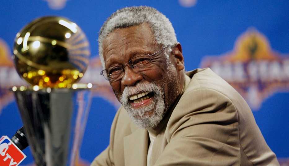 NBA legend Bill Russell laughing while sitting nearby the Larry O'Brien Championship Trophy