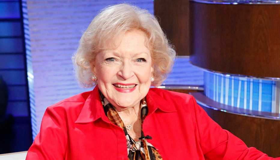 Betty White in a red shirt smiling on the set of the game show To Tell the Truth
