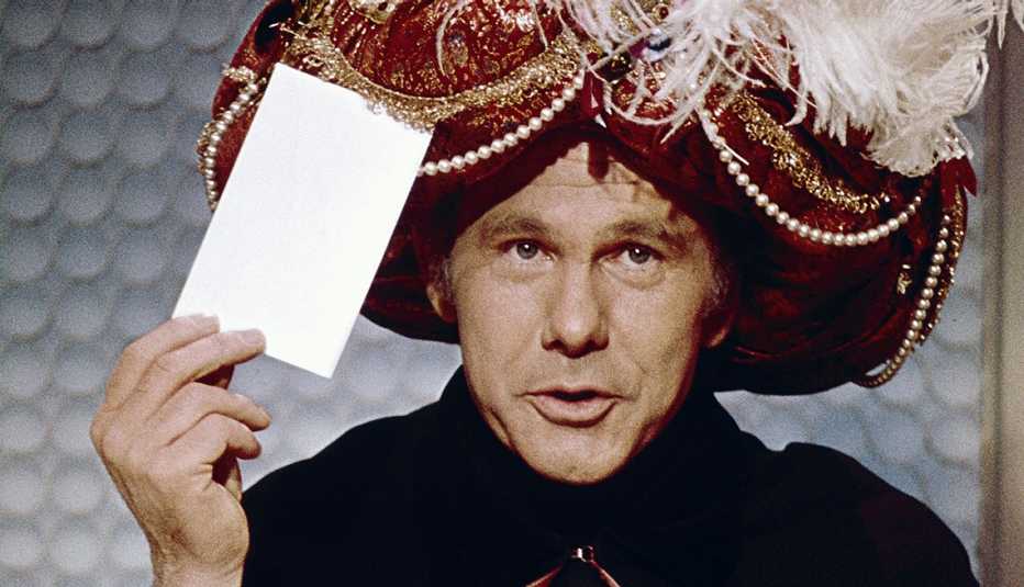 tonight show host johnny carson holds an envelope up to his turban while performing his iconic carnac the magnificent character