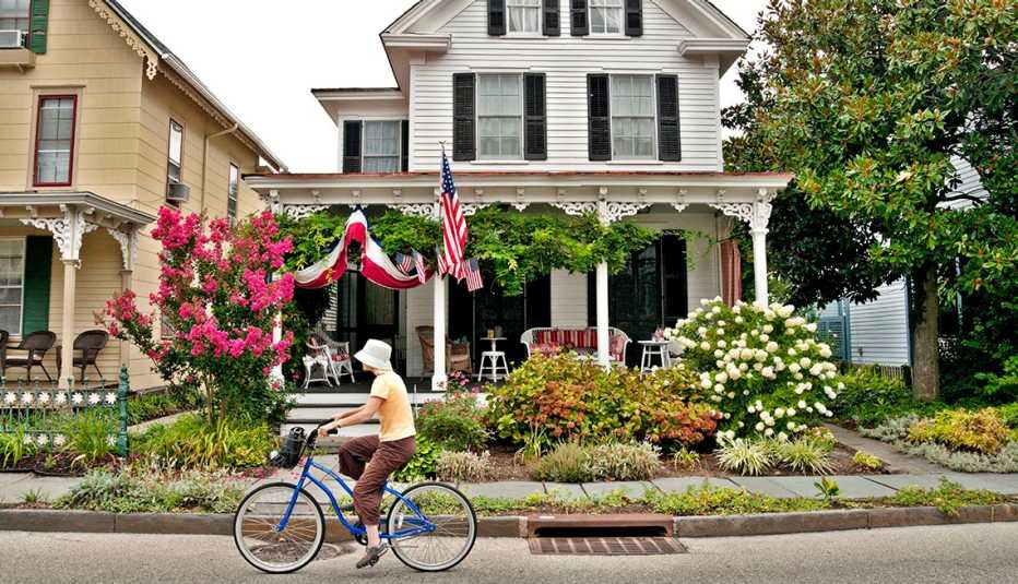 a woman rides a bicycle in front of a home decorated with flags and plants