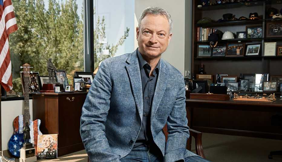 Gary Sinise in a window office with an American flag visible behind him, along with a guitar painted like an American flag and many picture frames on a desk and bookshelf