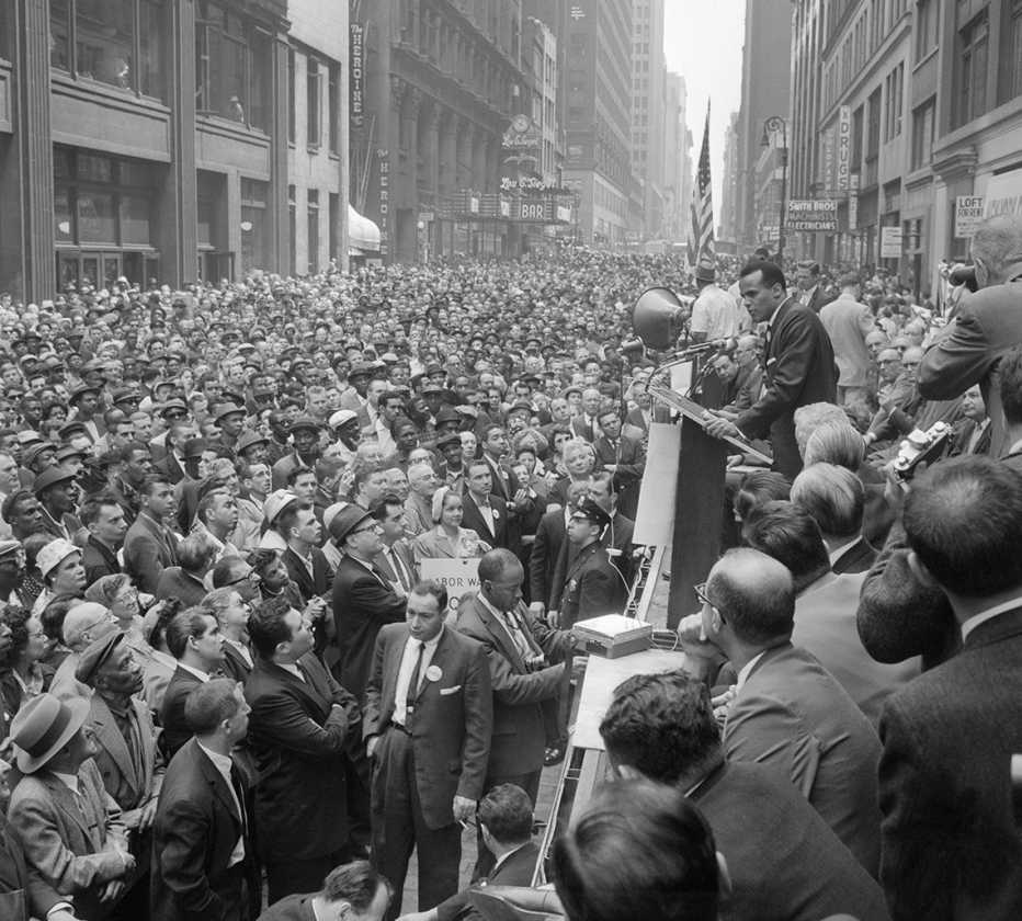 Harry Belafonte stands at a podium talking to a large crowd at a Civil Rights rally on West 38th Street in New York City