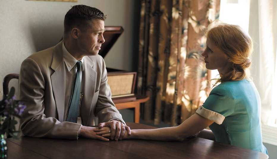 Brad Pitt and Jessica Chastain hold hands while sitting at a table in the film The Tree of Life
