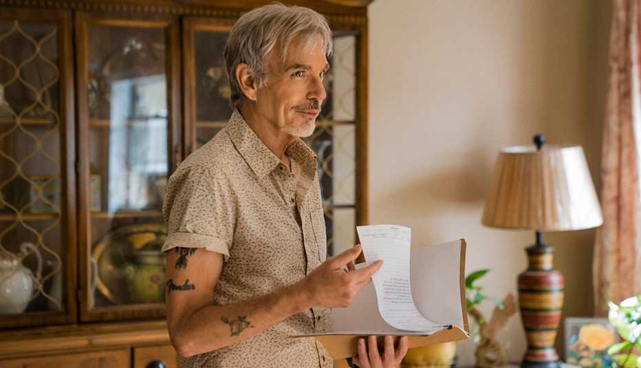 Billy Bob Thornton in character, standing in a living room holding a paper.