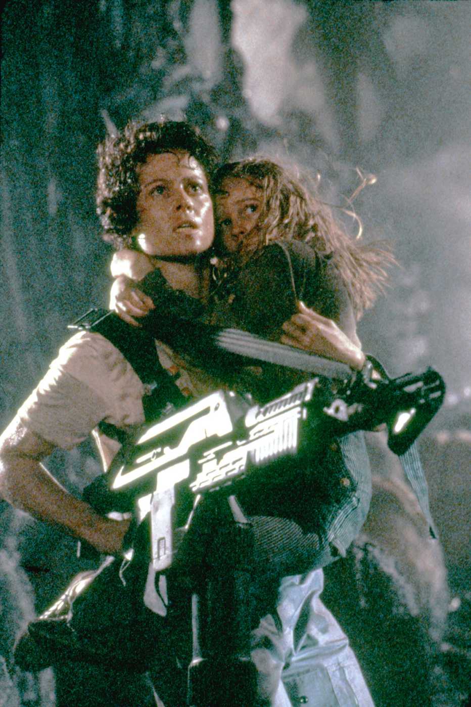 Sigourney Weaver holding an assault rifle holding Carrie Henn in her arm in the film Aliens