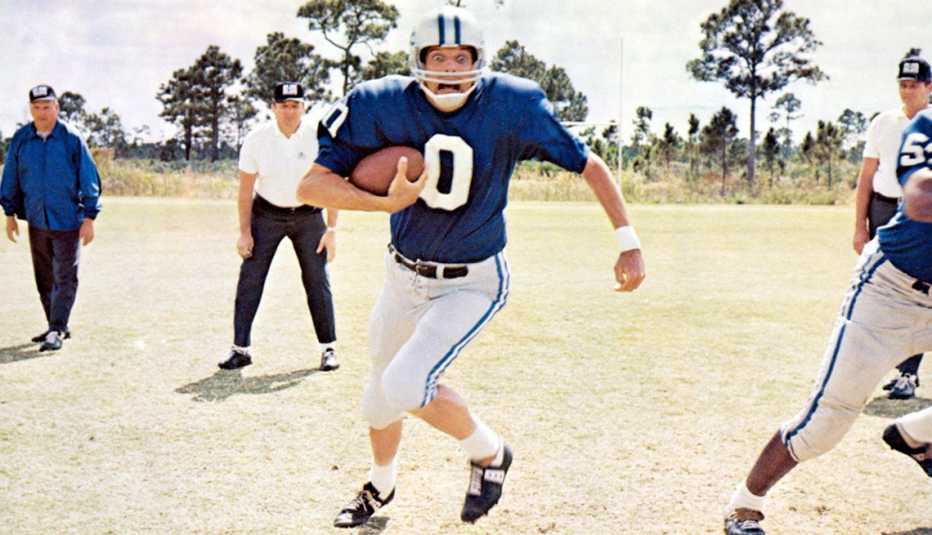 Alan Alda carrying a football with a worried look on his face in a scene from the film Paper Lion