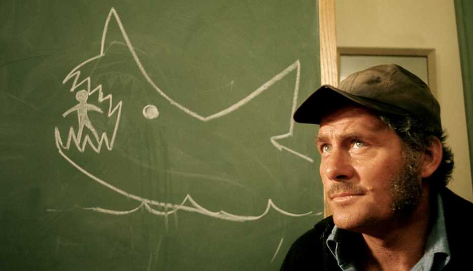 Actor Robert Shaw in front of a chalkboard showing a drawing of a shark eating a person