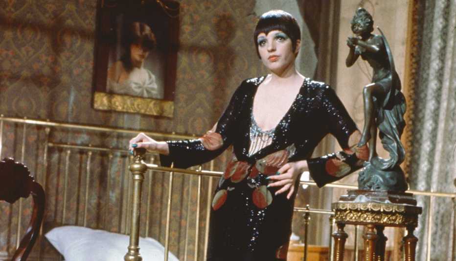 Liza Minnelli wearing a low cut long black dress posing beside a bed for the film Cabaret