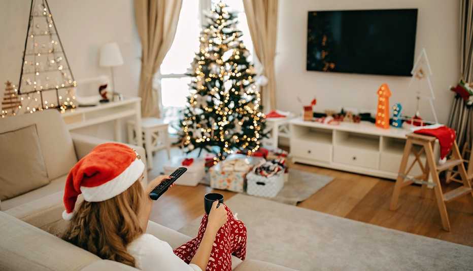 A woman wearing a Christmas hat is using a remote to turn on the TV during the holidays