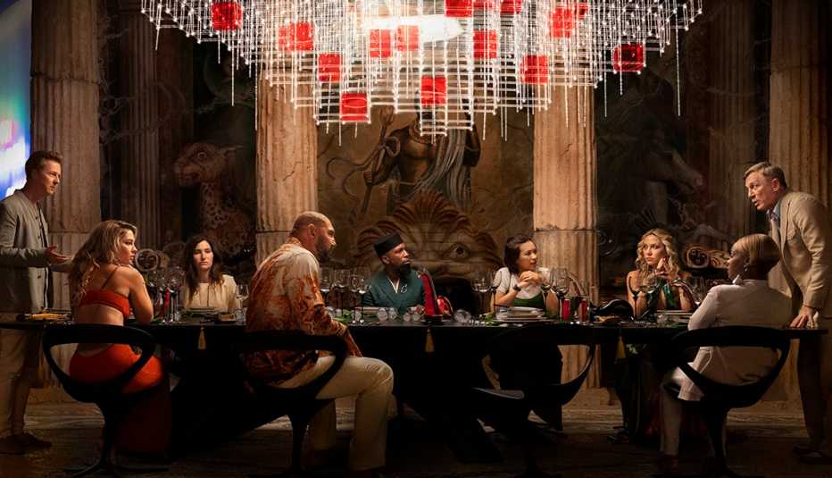 Edward Norton, Madelyn Cline, Kathryn Hahn, Dave Bautista, Leslie Odom Jr., Jessica Henwick, Kate Hudson, Janelle Monae and Daniel Craig together at a dinner table in the film Glass Onion: A Knives Out Mystery