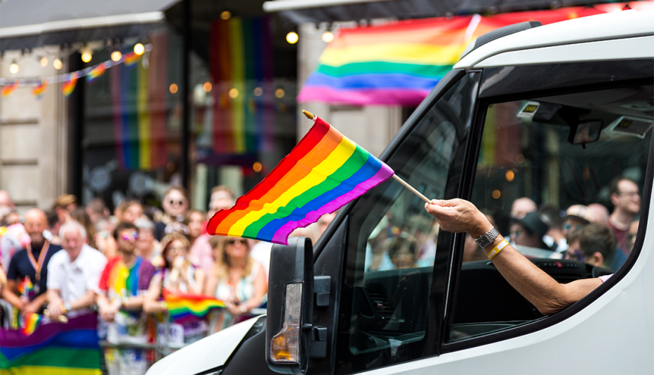 a person in a car sticking their hand out the window waving a rainbow flag at london pride in the united kingdom
