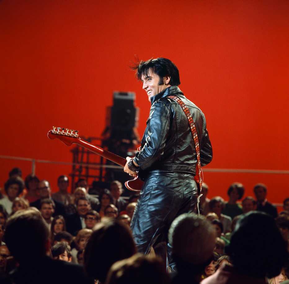 elvis presley smiles with his guitar as he stands in front of an audience during his 1968 comeback special