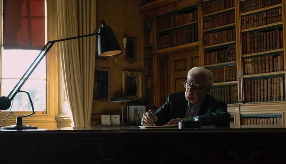 author john le carre writing at a desk inside a room with a large bookshelf