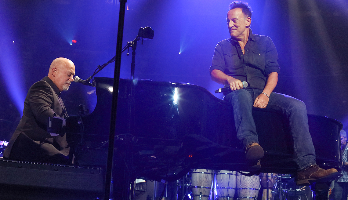 Billy Joel playing the piano as Bruce Springsteen sits on top.