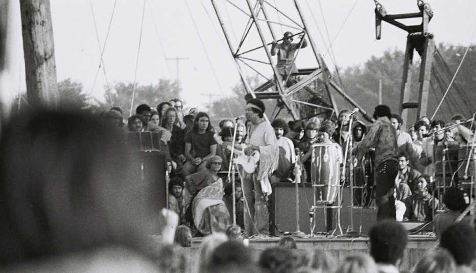 Jimi Hendrix and band onstage at Woodstock from the point of view of the crowd, with a partially obstructed view of the back of people's heads