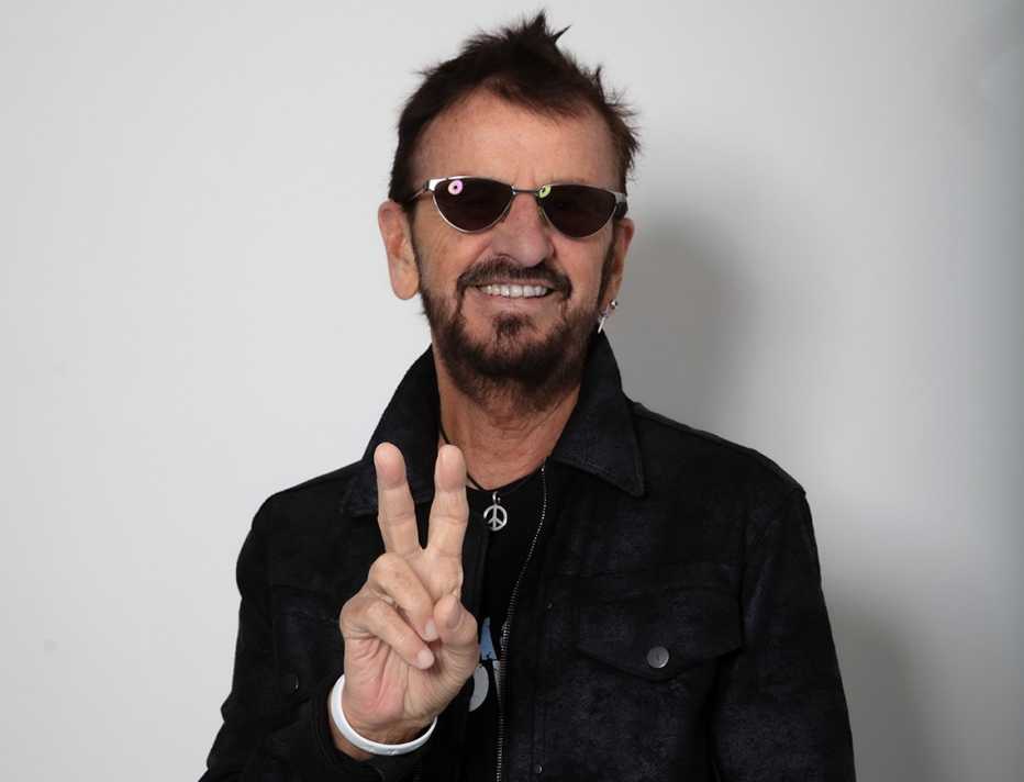 Ringo Starr wearing sunglasses while giving the peace sign