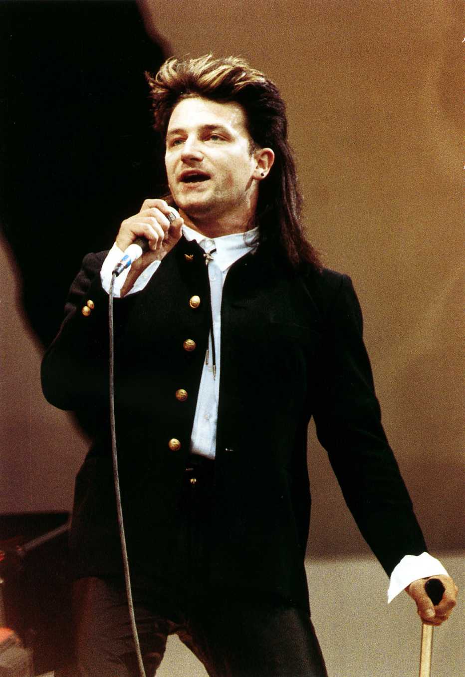 Bono holding a microphone while performing onstage at Live Aid in Wembley Stadium