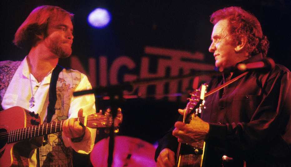 Johnny Cash playing his guitar onstage with his son John Carter Cash who is always playing a guitar