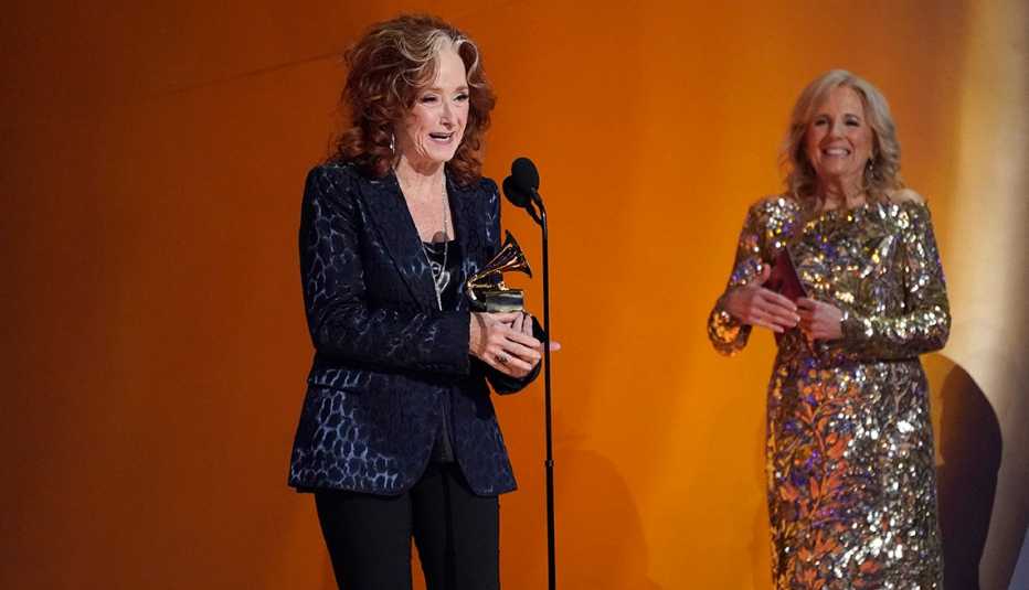 Bonnie Raitt speaks onstage after winning song of the year with First Lady Jill Biden looking on