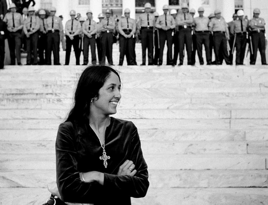 joan baez at the alabama state capitol in 1965 with police officers standing on the steps behind her