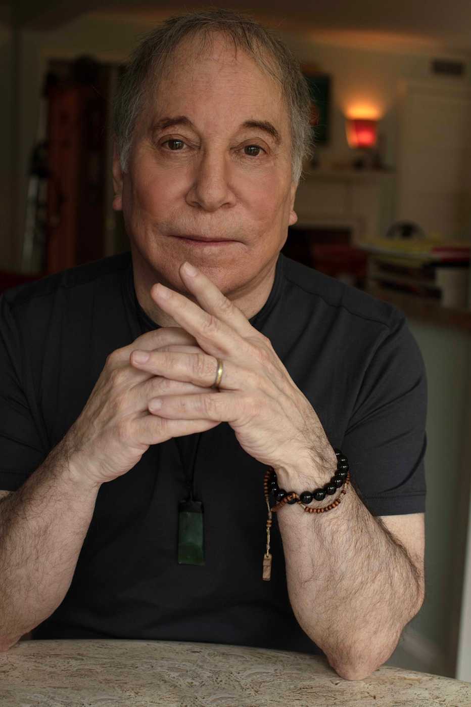 Musician Paul Simon sitting at a table with his hands clasped