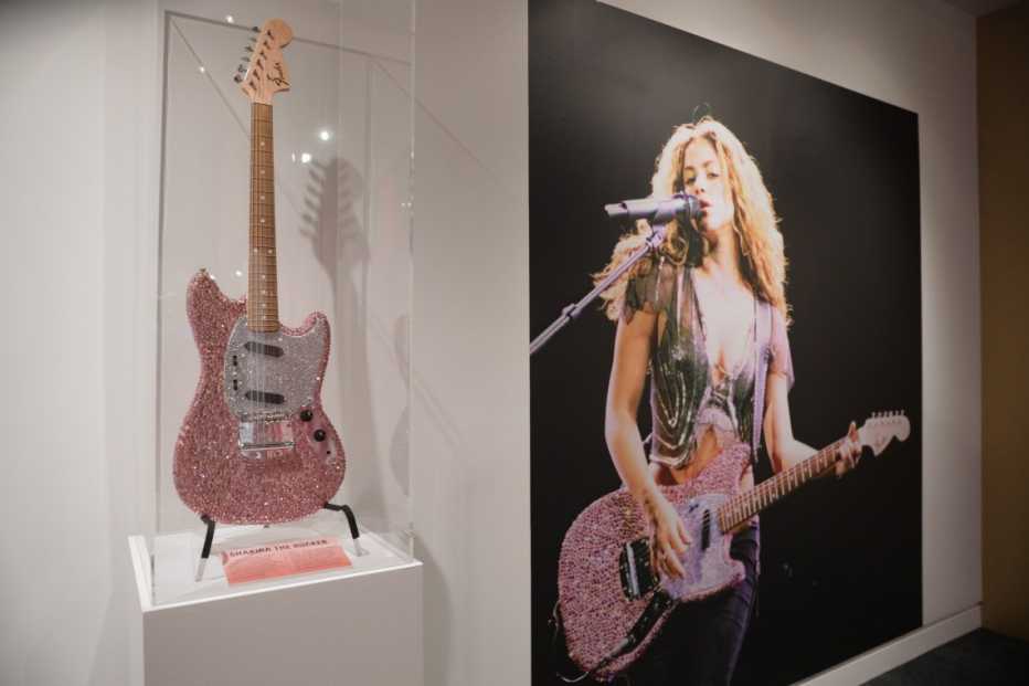 A pink guitar next to a photo of Shakira playing that guitar during a performance on display at the Shakira, Shakira: The GRAMMY Museum Experience