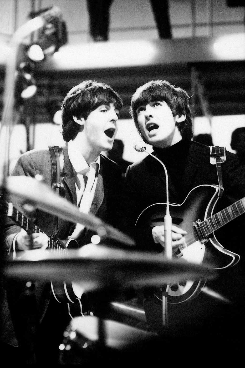 Paul McCartney and John Lennon sing into a shared microphone during the Beatles rehearsal for a television special at Wembley Studios