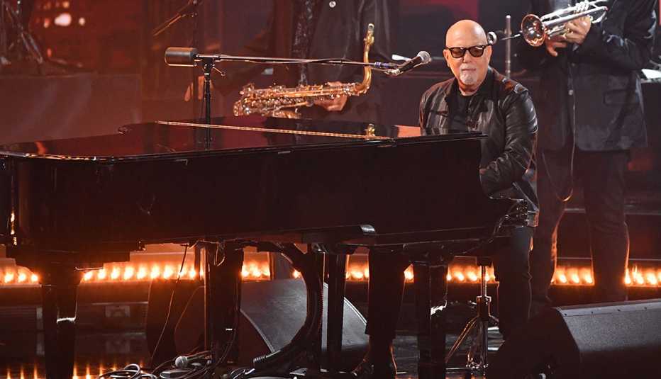 Billy Joel sitting at a piano performing onstage at the 66th Annual Grammy Awards