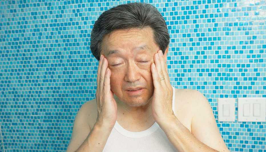 Asian man rubbing his temples in bathroom, Symptoms
