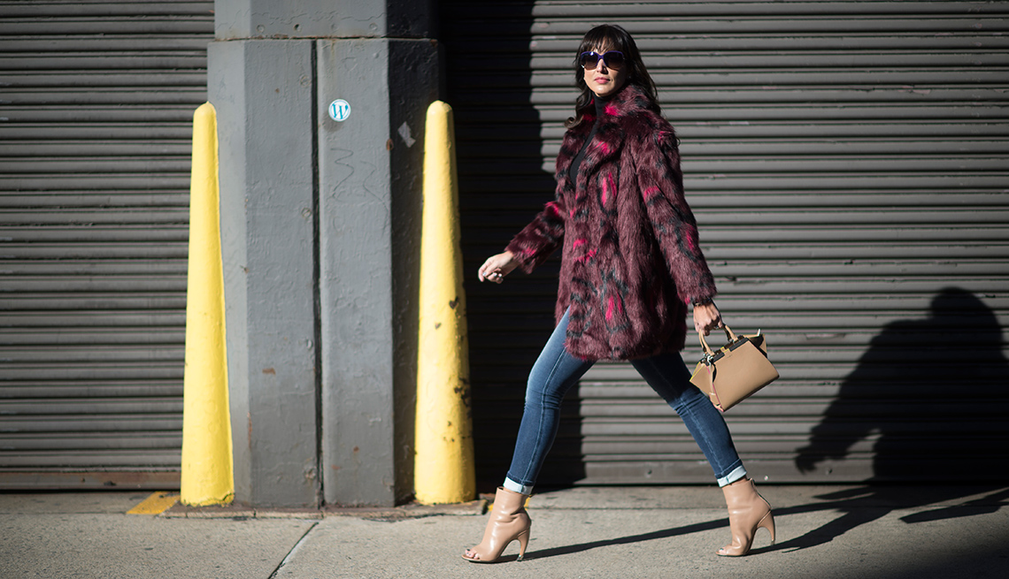 Woman walking on sidewalk in light, maroon and black coat, jean leggings, tan shoes and purse